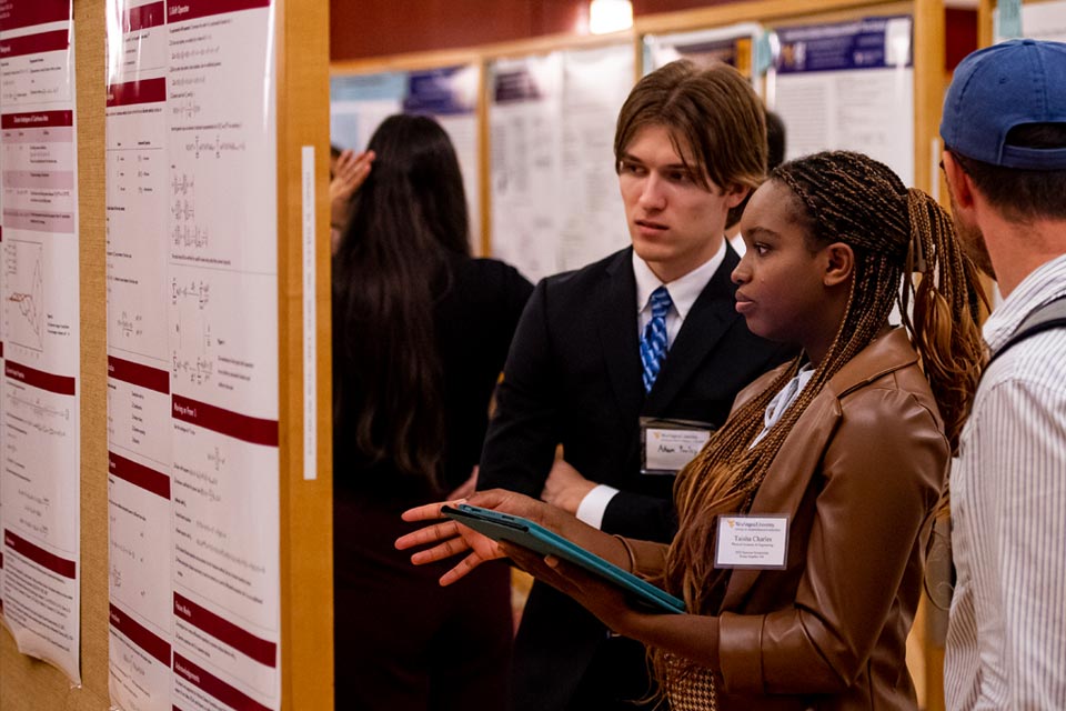 A white male student and a black female student discuss a research poster